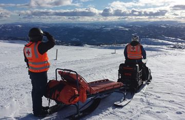 To menn far hjelpekorpsett på scooter med hvitkledd fjelllandskap i bakgrunn