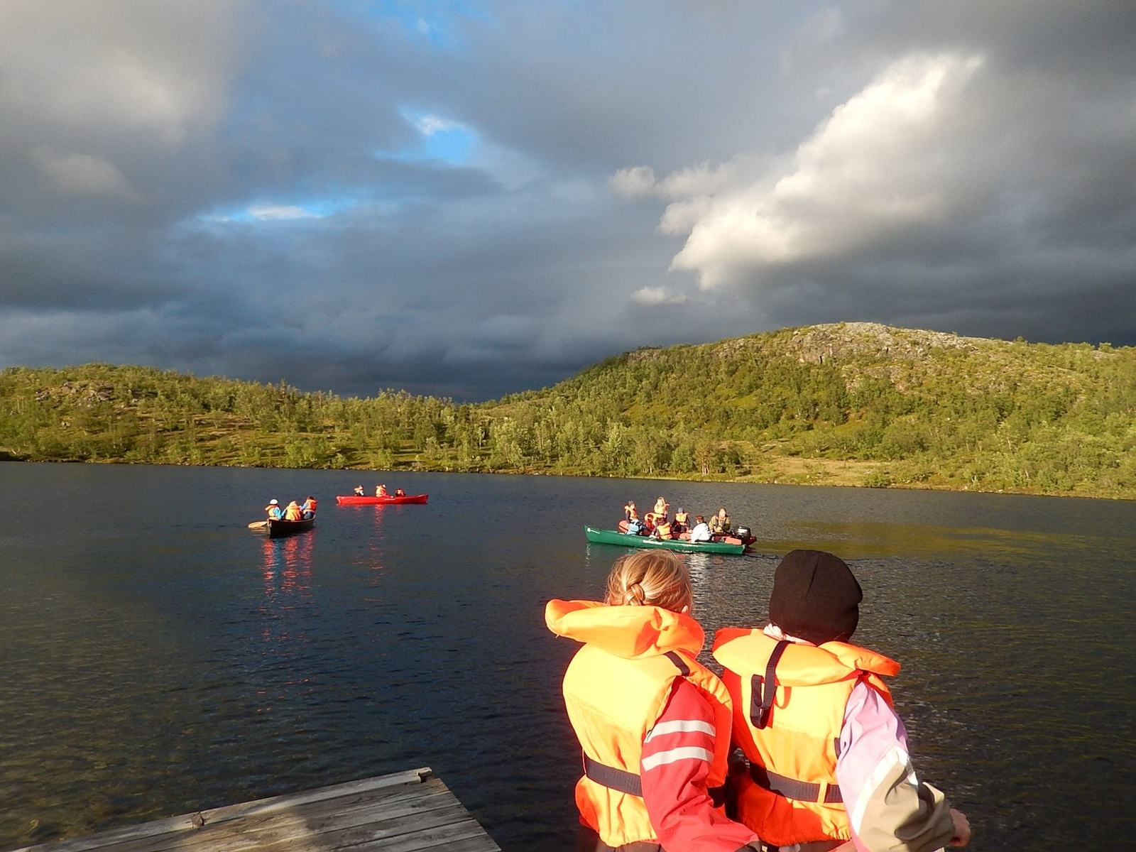 Ryggen til to som er på kanotur. Man ser flere kanoer og elva i bakgrunnen.