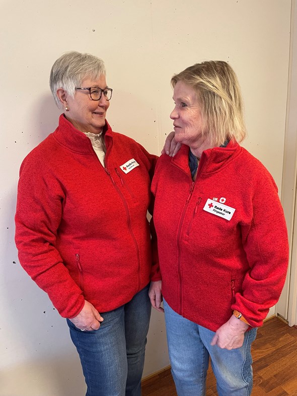 To kvinner i Røde Kors-jakker ser på hverandre og smiler