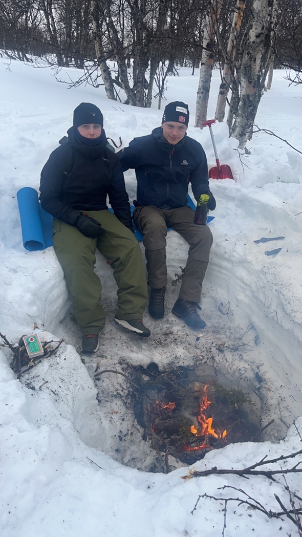 To ungdommer ved et bål ute i skogen på vinteren.