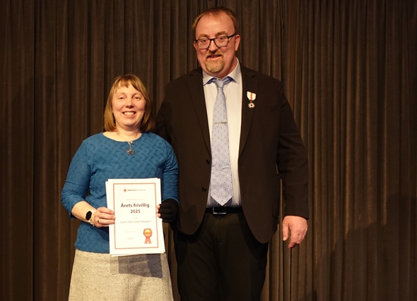 Kvinne står på scene og har fått tildelt pris av en mann.