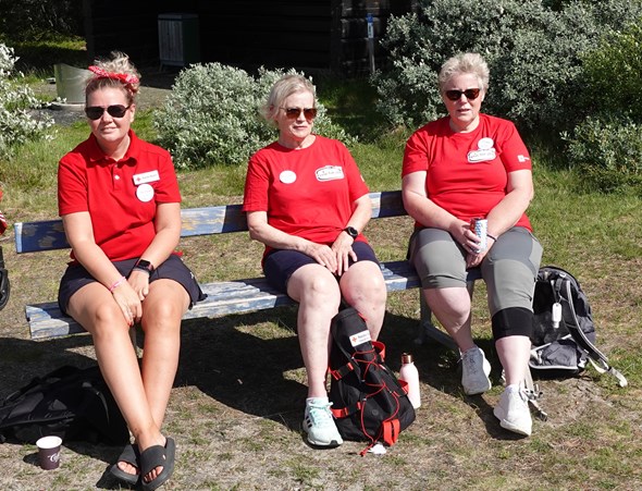 Tre frivillige i Røde Kors-klær på en benk på stranda