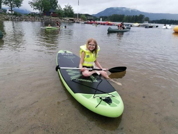 Jente på padlebord på vannet med redningsvest