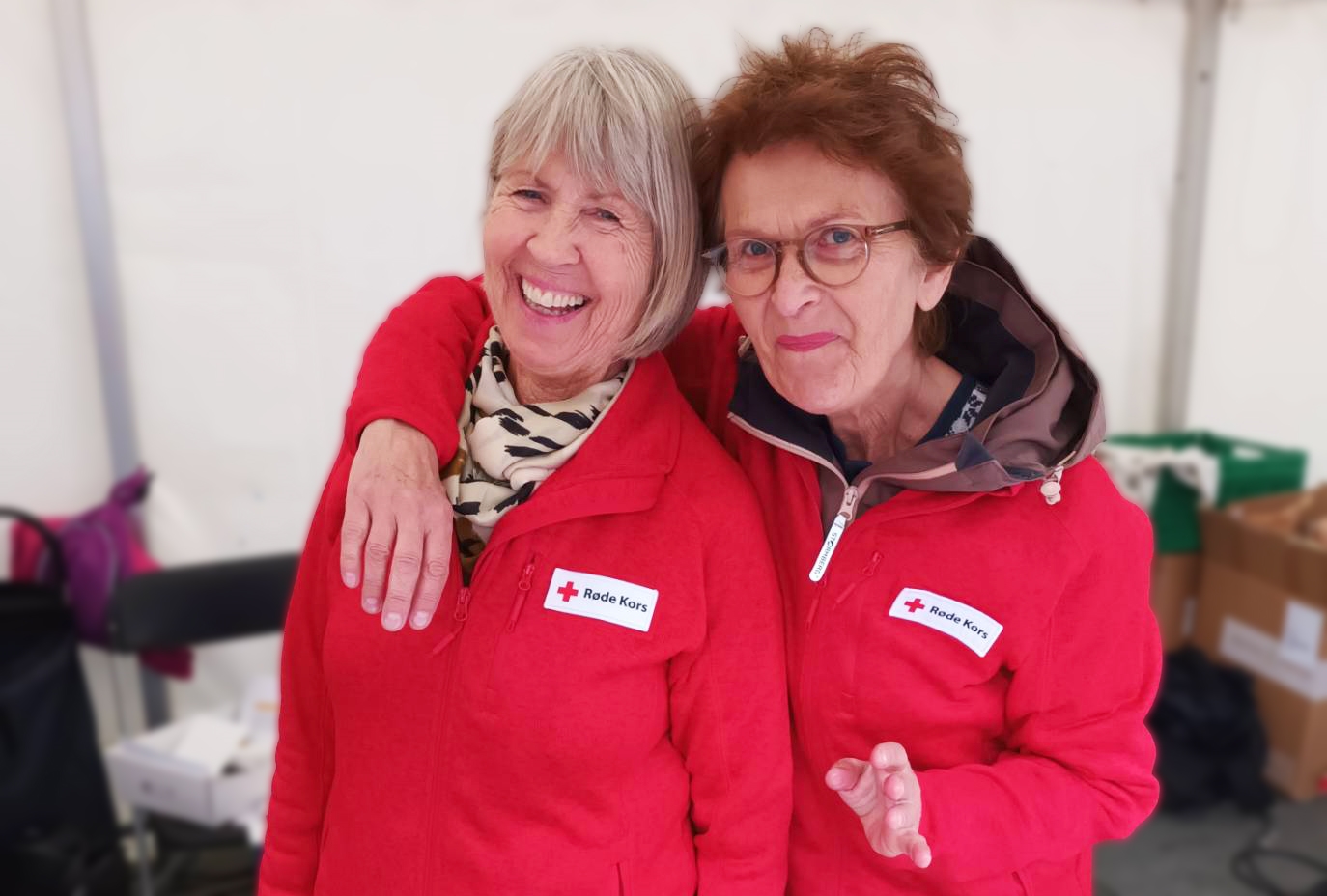 To besøksvenner og frivillige i Bergen Røde Kors på stand iført Røde Kors-jakker. 