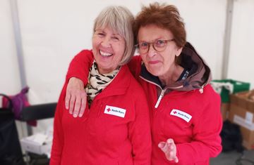 To besøksvenner og frivillige i Bergen Røde Kors på stand iført Røde Kors-jakker. 