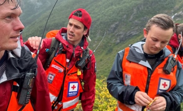 Tre frivillige i Røde Kors står på toppen av en høye og tar en pust i bakken etter en krevende klatretur.