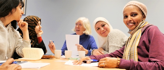 Fire damer sitter rundt et bord og får undervisning i norsk fra en frivillig norsklærer i Røde Kors. 