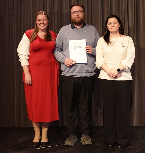 En mann står med diplom mellom to kvinner på en scene.