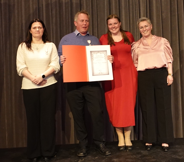 Fire personer står på en scene, den ene mannen har fått Norges Røde Kors Fortjensmedalje