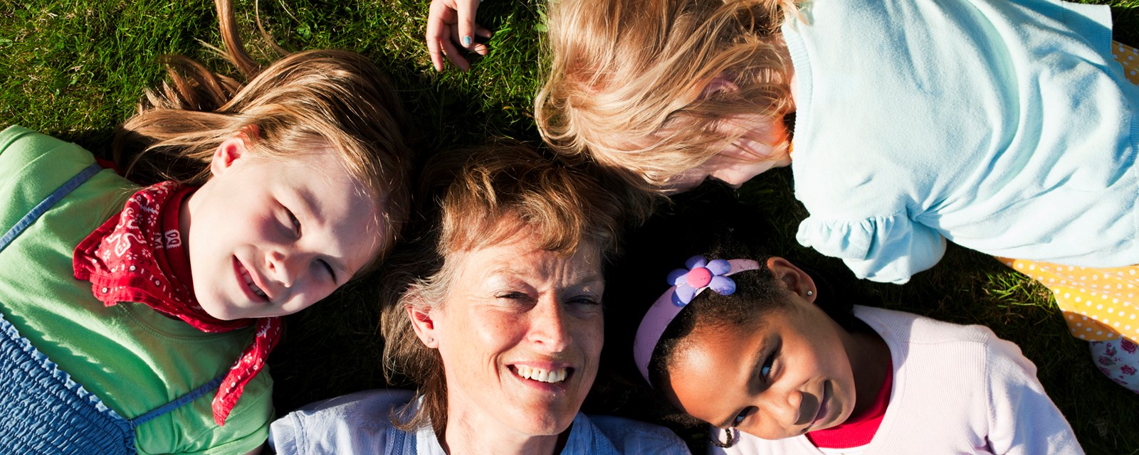En voksen dame og tre barn ligger og smiler i gresset i Botanisk hage