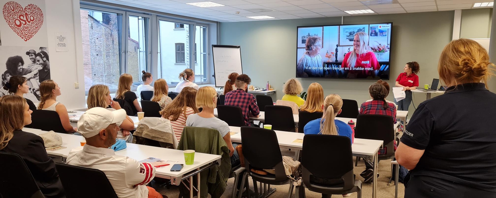 En frivillig foredragsholder holder introduksjonskurset for nye frivillige i en fullsatt sal