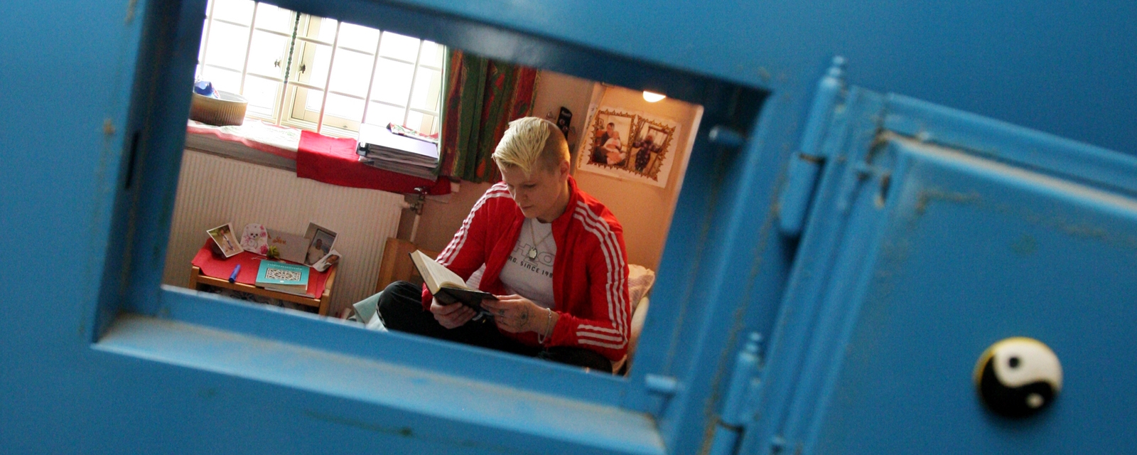 En ung jente som sitter og leser. Vi ser henne gjennom luken i en fengseldør