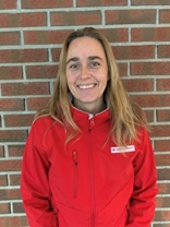 Kvinne med lyst langt hår i rød jakke, mot vegg, ute