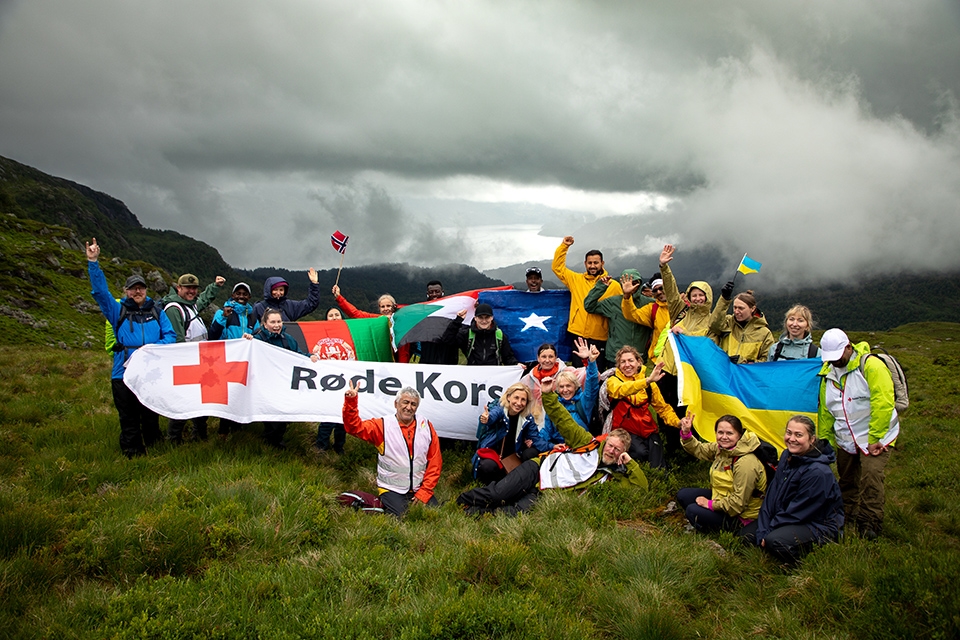 En gruppe personer oppstilt, vifter med flagg. Fjell og fjord i bakgrunne.