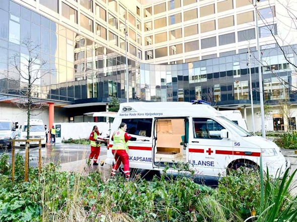 To personer står ved en beredskapsambulanse foran et moderne bygg med store glassfasader.