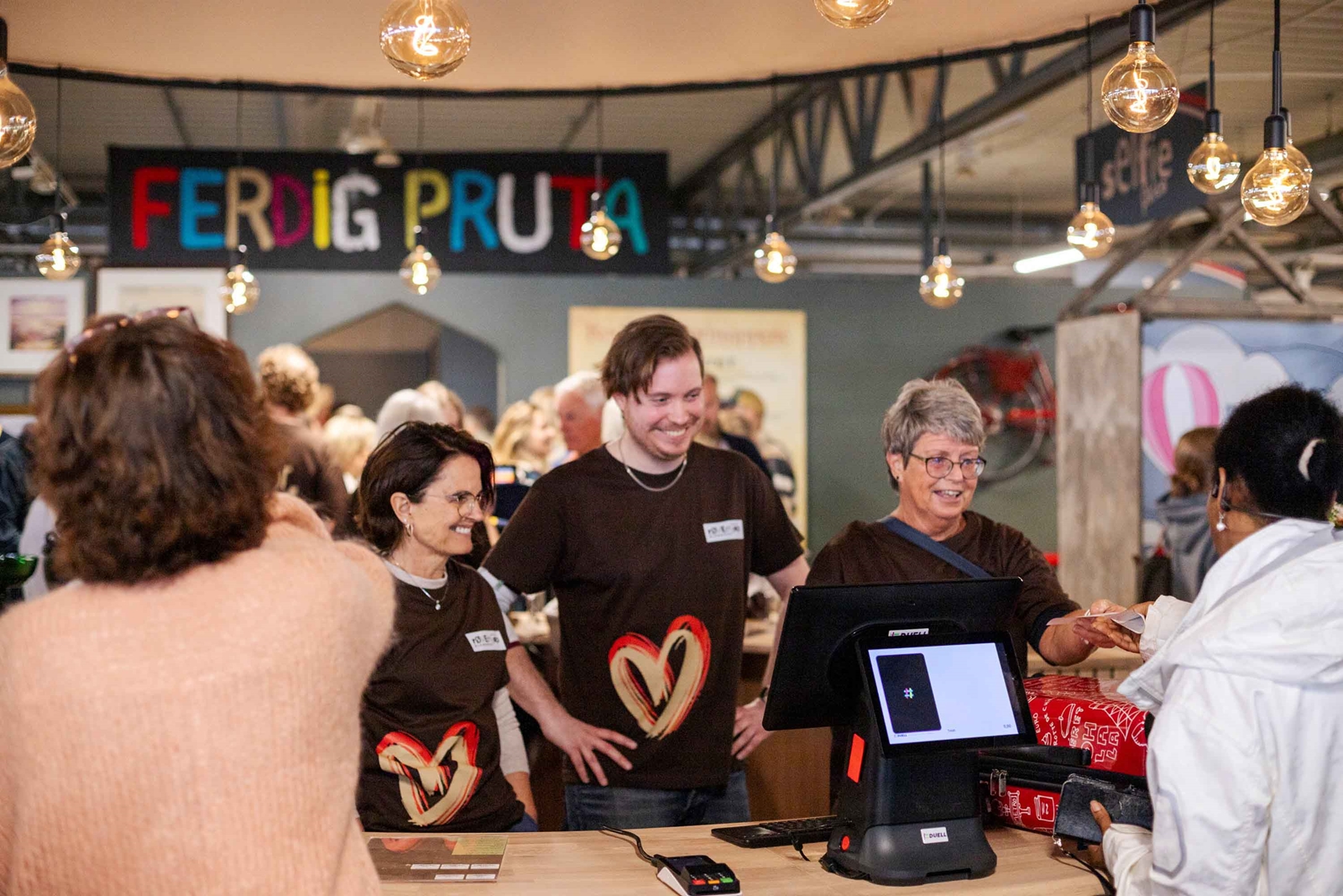 Tre smilende personer i kassen på gjenbruks-butikken.