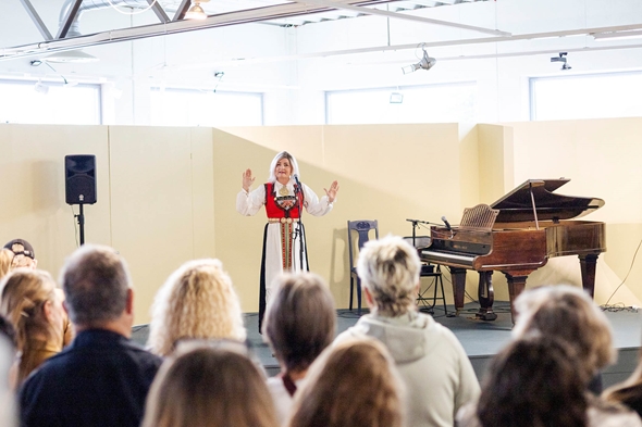 Kvinne i bunad på scene foran mennesker