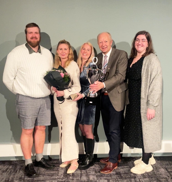 Fem smilende personer med blomster og pokal.