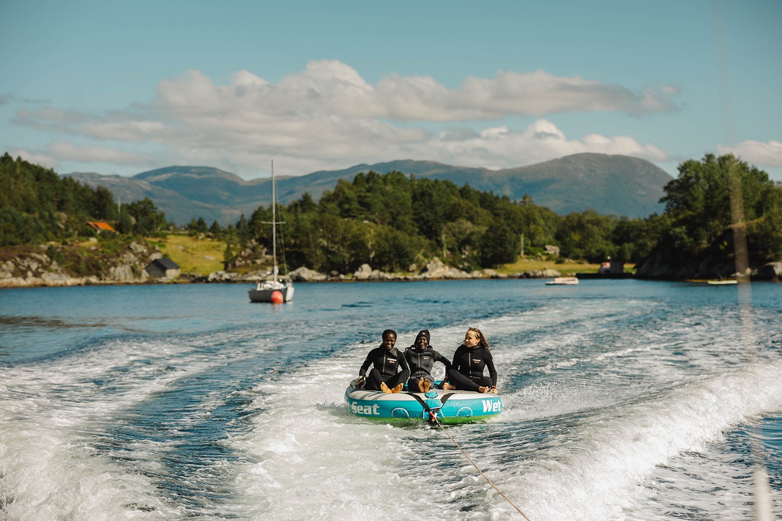 Tre jenter i tube bak båt omringa av fjordlandskap