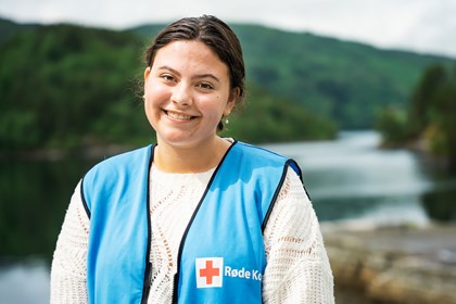 Ung jente i blå Røde Kors vest framfor fjordlandskap.