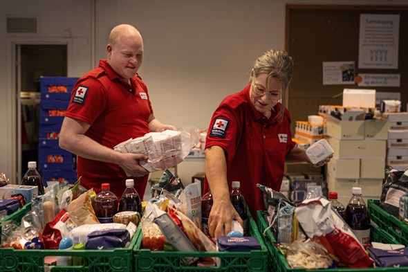 Ein mann og ei kvinne i røde kors t-skjorte putter mat i kasser.