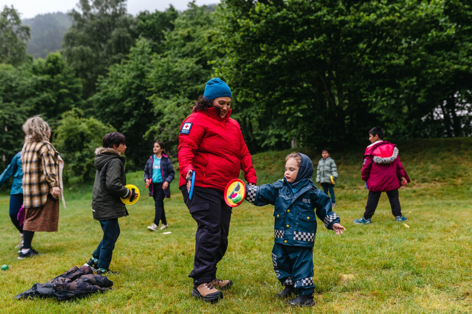 Dame i Røde Kors-jakke leikar med barn