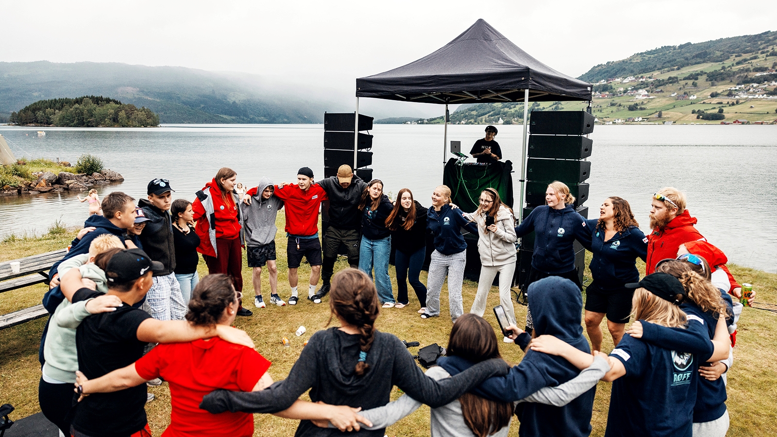 Unge menneske står i ring framfor vakker natur og ein DJ i telt. 