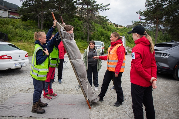 Ei gruppe menneske løftar opp ei båre med ei jente som smiler.