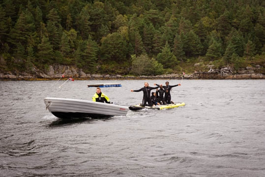 Ein glad gjeng med born sit på eit SUP-brett som blir dratt av ein båt.
