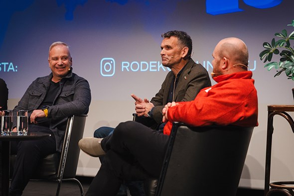 Tre menn snakkar og smiler i ein uformell sofaprat.