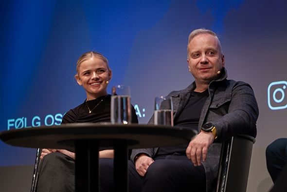 Ei kvinne og ein mann sit i ein sofa og smiler.