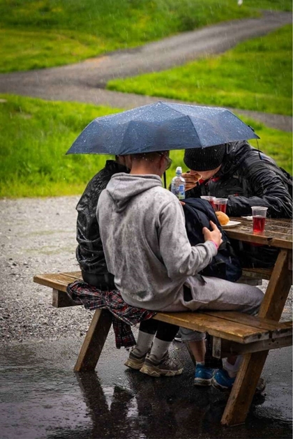 Deltakarar sit ute på ein benk under ein paraply og et burgarar.