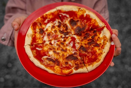 Ei jente held opp eit fat og viser ein liten pizza.