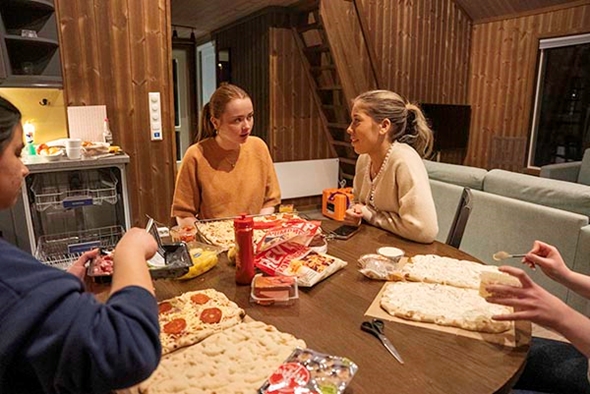 Fire jenter sit ved eit bord og lagar pizza ilag.