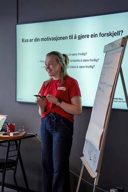 Ei kvinne står ved ei tavle og smiler.