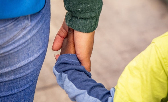 Nærbilde av ei hand som held eit lite barn si hand.