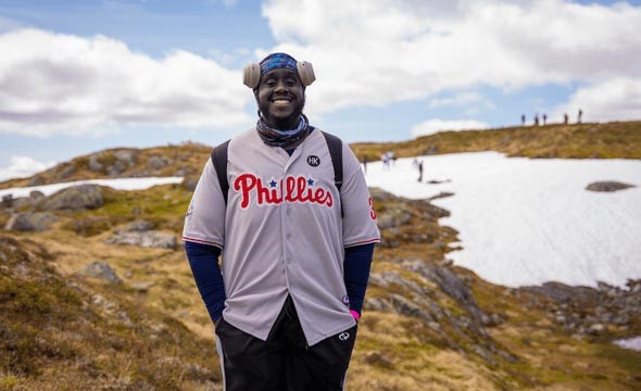Ein deltakar smiler på toppen av fjellet. Det er sol og vid utsikt i bakgrunnen.