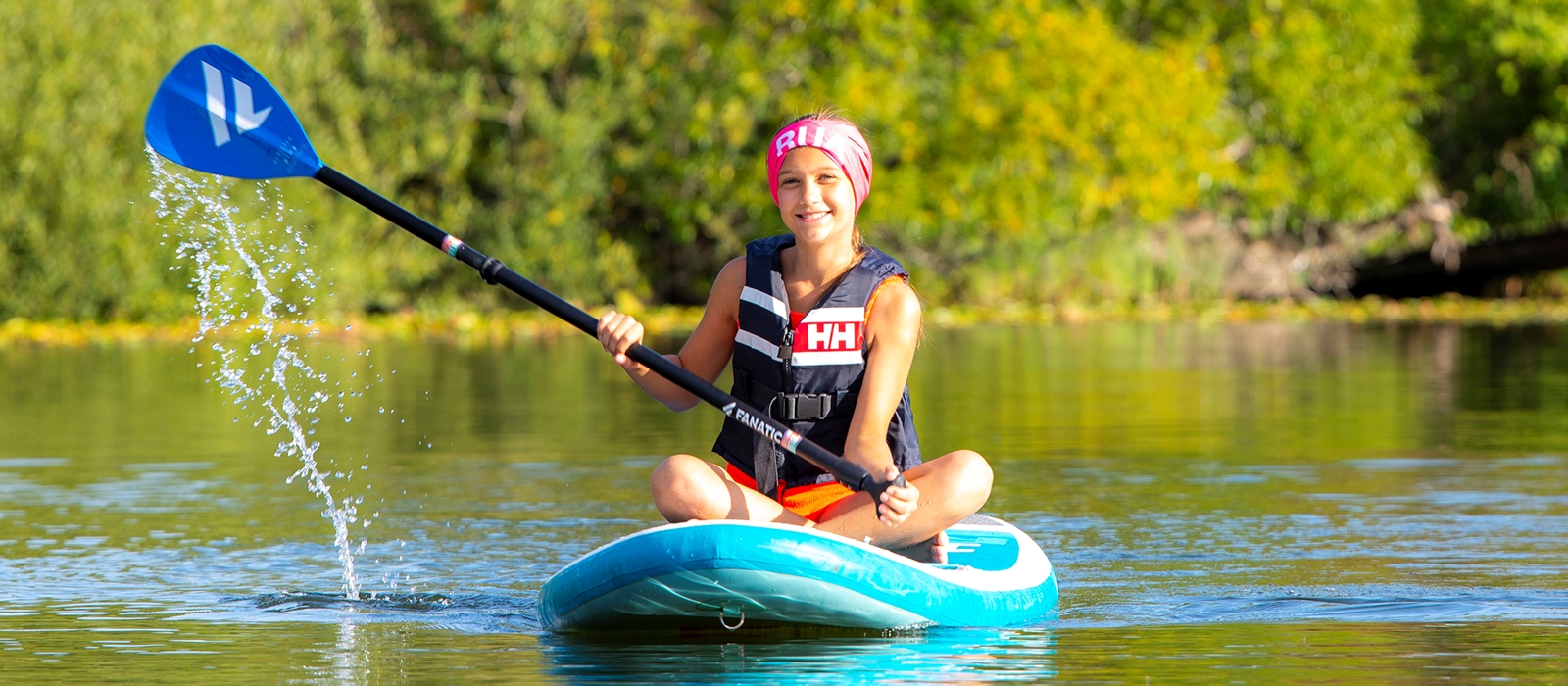 Jente padler sittende på SUP-brett.