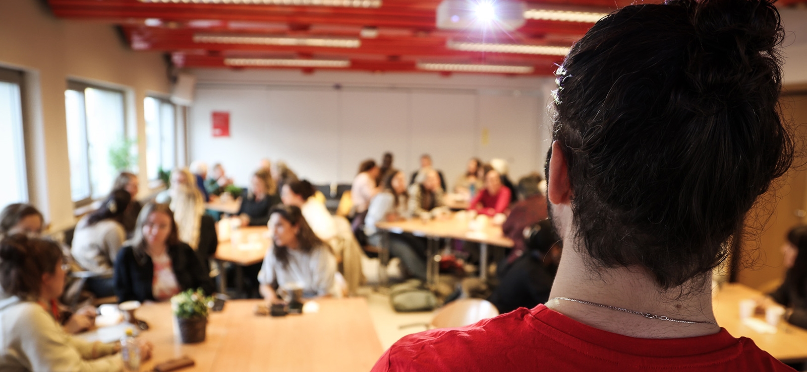 Kursholder i fokus med et rom fylt med kursdeltagere