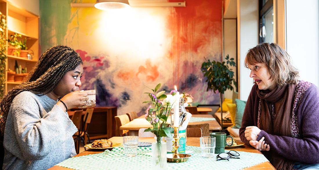 Frivillig mentor sitter på kafe med ungdom å drikker kaffe og prater sammen.