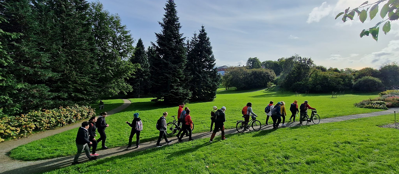 Turgruppa går på rekke i et grønt sommerlandskap.