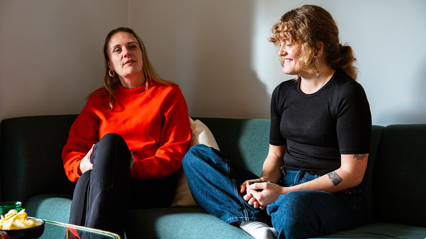 To damer sitter sammen i en sofa og prater.