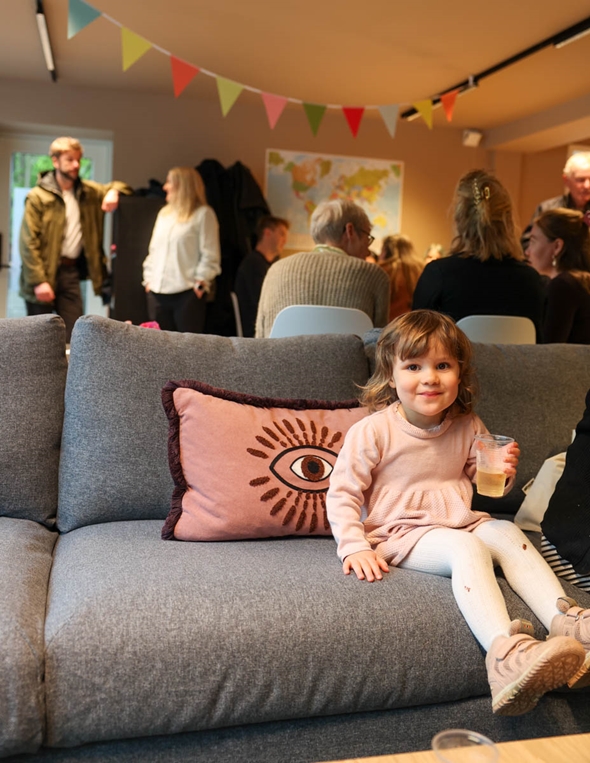 Full hus på åpningsdagen til Mosaikk-åpen møteplass. I forgrunnen sitter en liten jente og koser seg i sofaen.