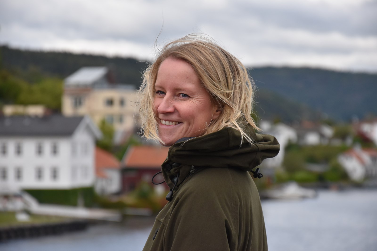 Anja (40) er frivillig leder i Siljan Røde Kors og aktiv i Skien Røde Kors hjelpekorps. Her står hun på Porsgrunnsbrua og smiler. Været er lett overskyet og det blåser. 