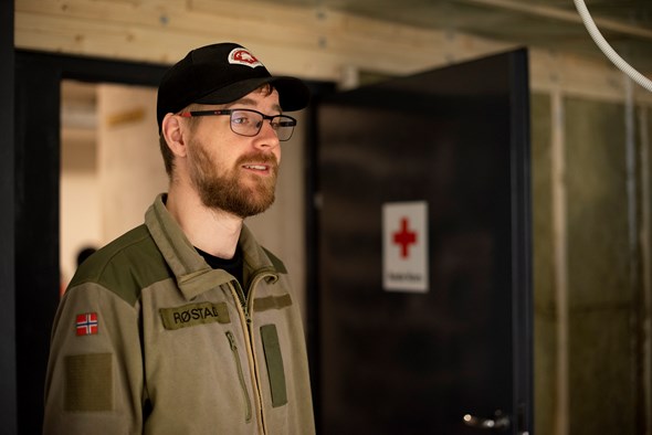 Portrett av en mann som står inne i et rom med Røde Kors-logo på døra. Han smiler.
