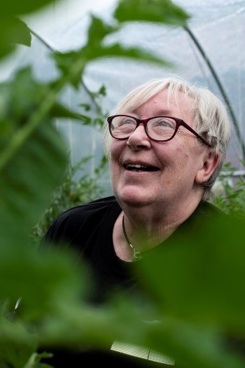 En dame smiler mellom tomatplanter i et drivhus