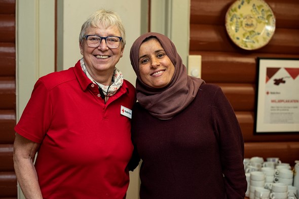 En dame i Røde Kors-klær og en dame med hijab står og smiler mot kamera.