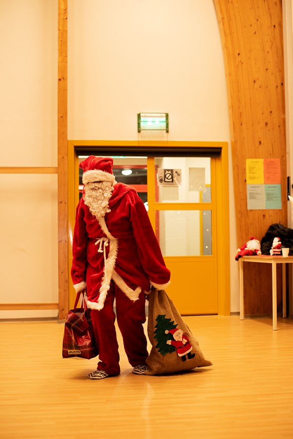 En julenisse står midt på et gulv med to julesekker
