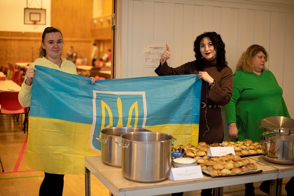 to damer står foran et bord med mat og holder et ukrainsk flagg mellom seg.