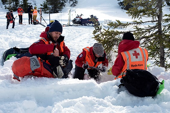 Tre mannskap fra hjelpekorpset sitter i snøen og graver et hull i snøen.
